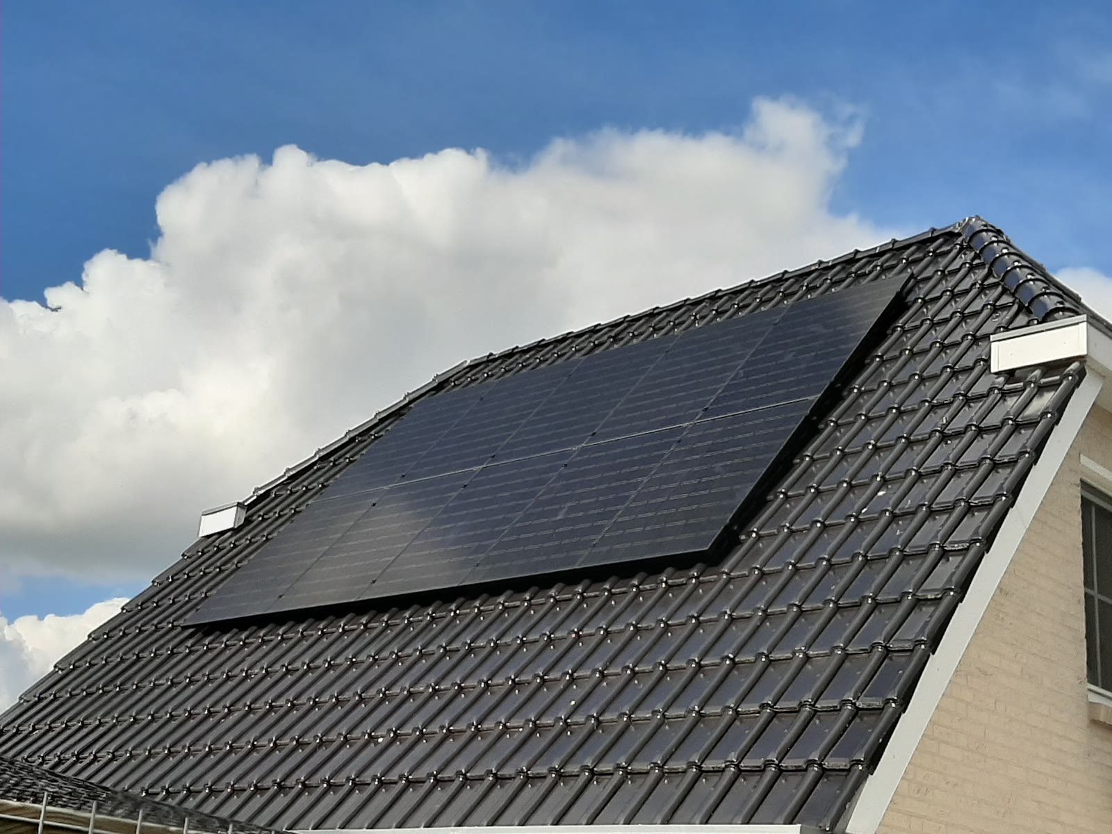 Full black zonnepanelen op een pannendak onder een wolkenlucht